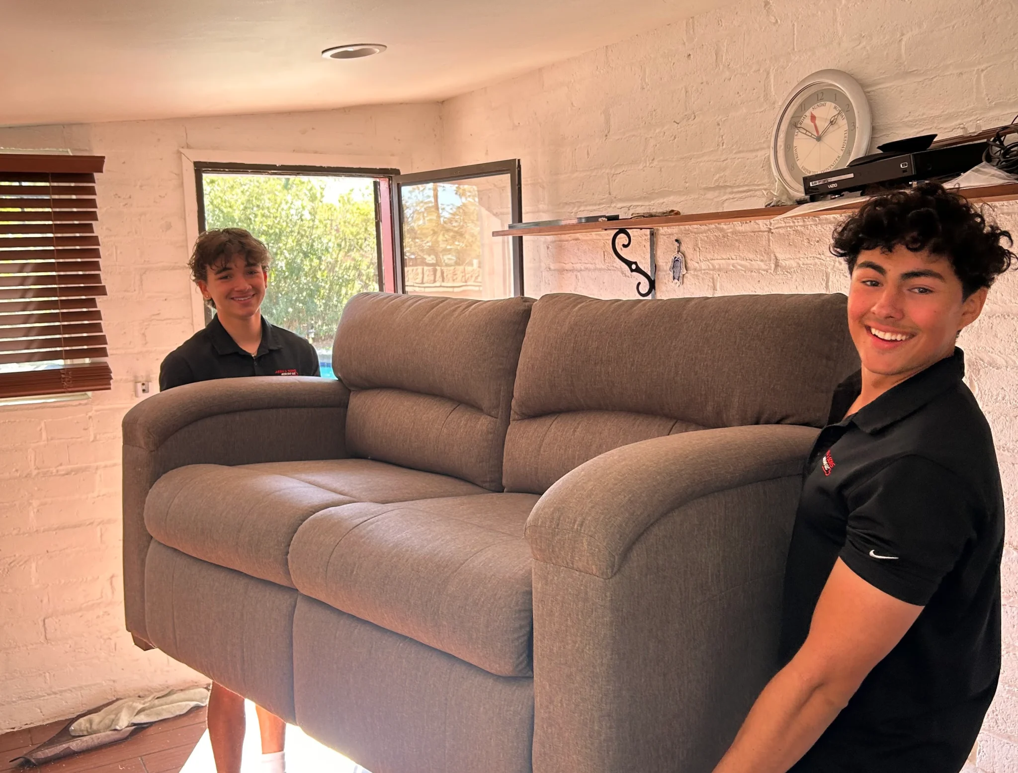 Two Abba and Sons Moving team members smiling while carefully carrying a couch during a residential move in Tucson